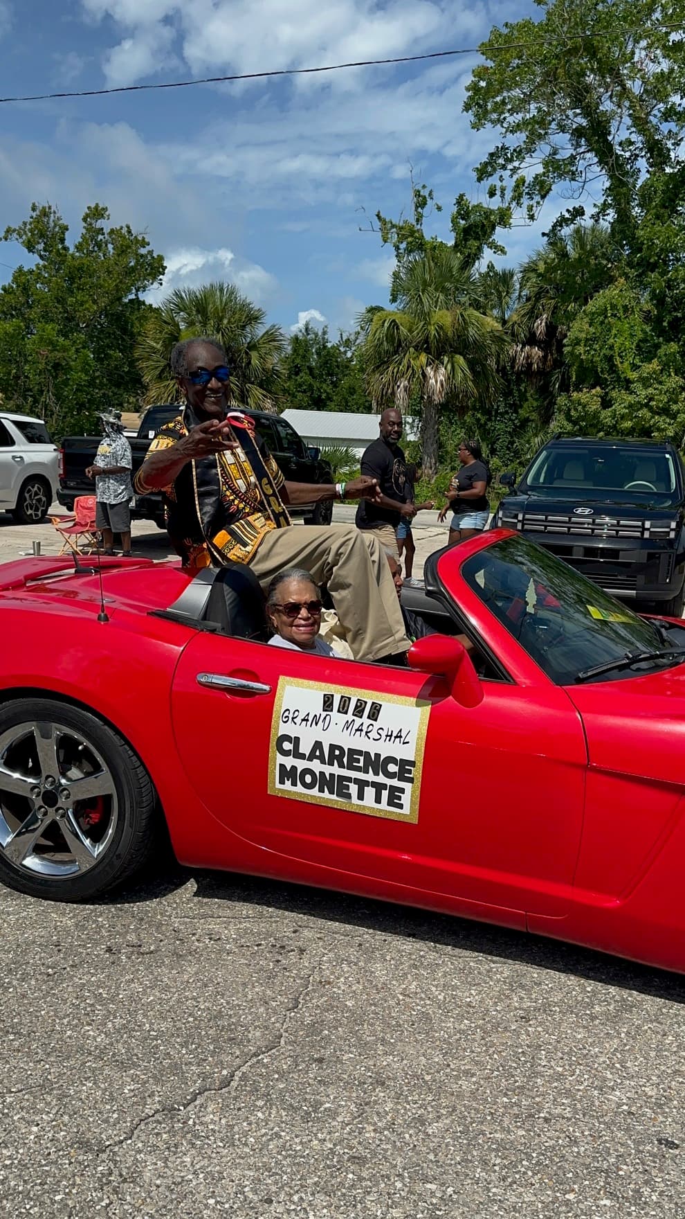 Grand Marshal Clarence Monette waving from a red convertible in the Juneteenth parade