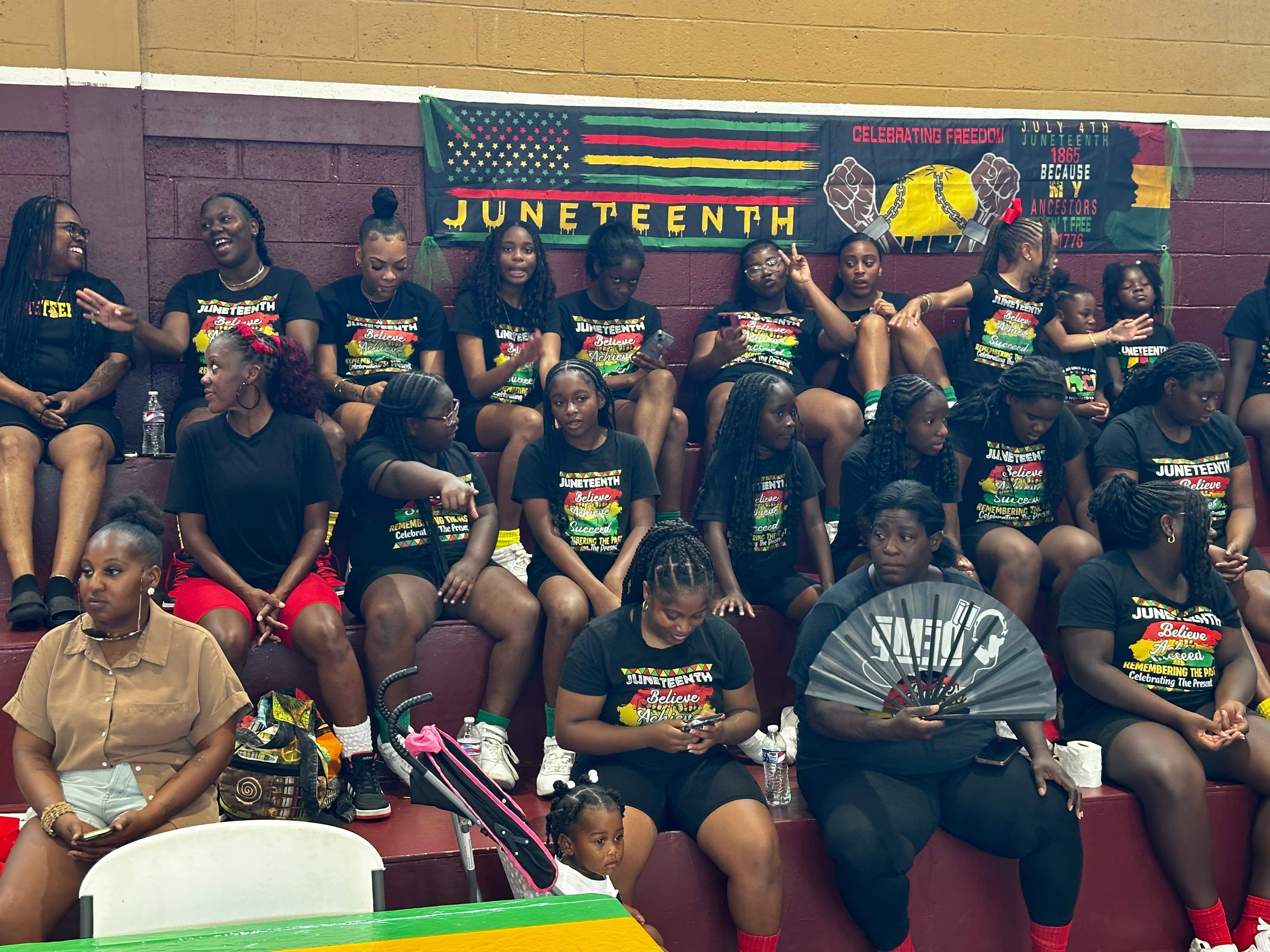 Large group of youth in matching Juneteenth t-shirts seated in the bleachers at Washington High School